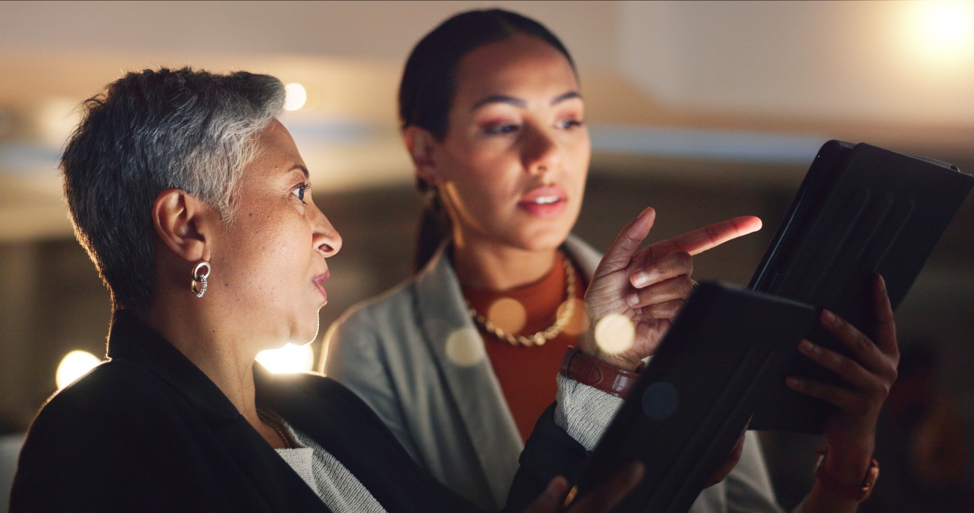 Mentor, training and employee working on a night project with manager helping with digital tablet or online strategy. Corporate, talking and business women planning together for company development